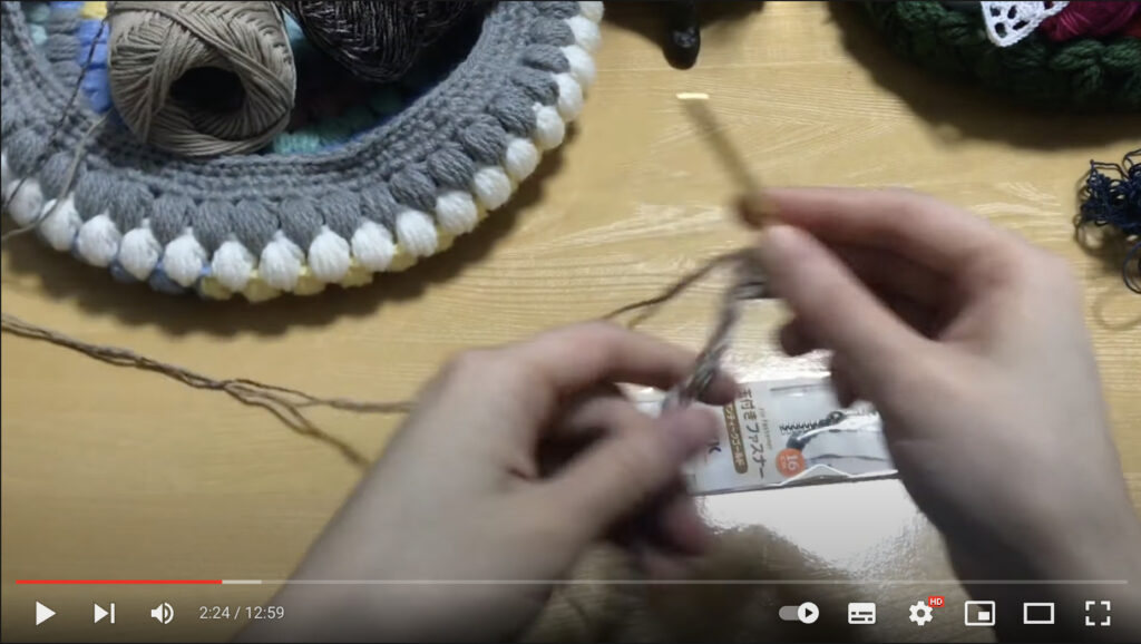 女性が右手にかぎ針を持って、グレーの毛糸を編み上げて行っているようすを写した写真。ペンケースの1段目を編んでいます。