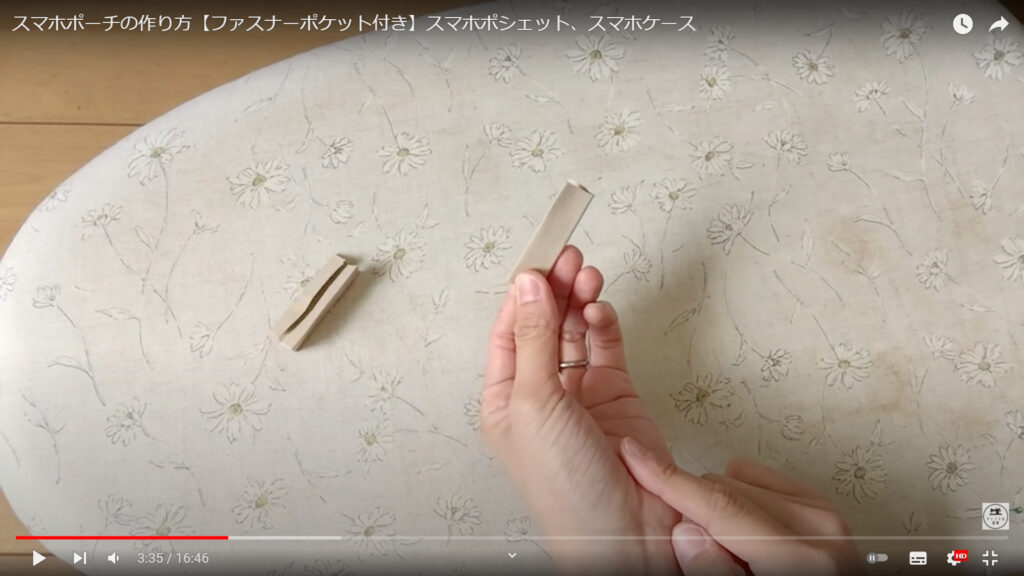 スマホケースのタグを作る作業を解説している動画で、折ったタグの生地を手にした画像。