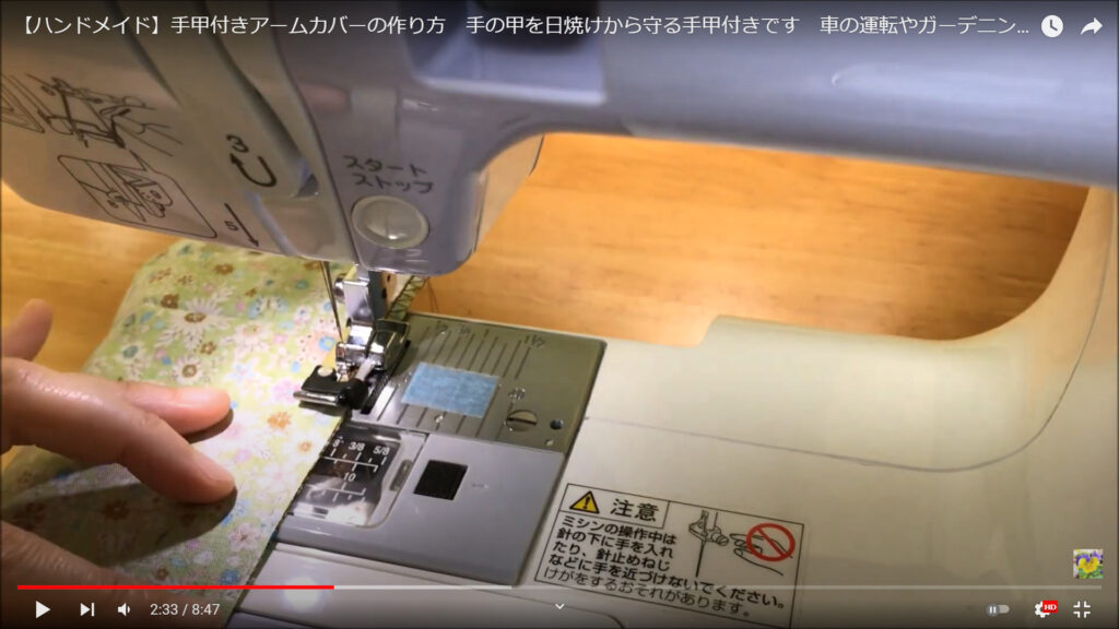アームカバーのサイドの部分を縫う作業を解説している動画で、布をミシンの機能「断ち目かがり」を使って縫う様子を表示した画像。