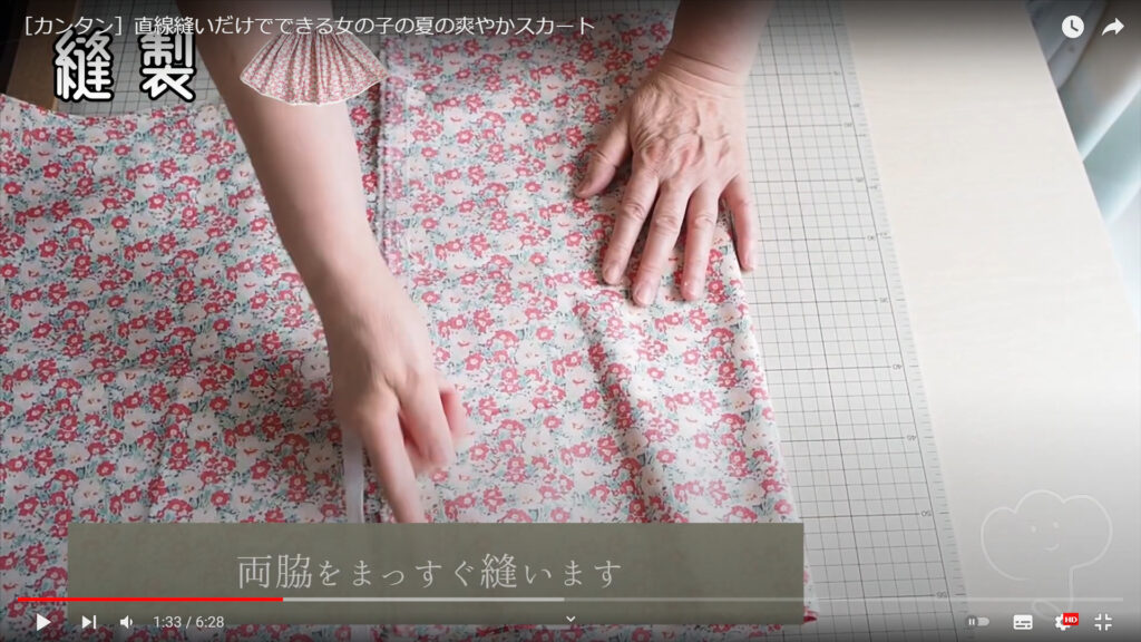 生地を裁断して縫う作業を解説している動画で、裁断した生地を合わせ、縫う箇所を指で指している様子と共に、「両脇をまっすぐ縫います」という文が表示された画像。