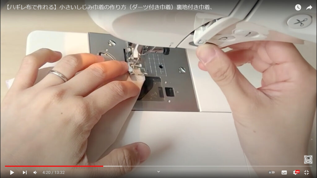 生地を縫い合わせる作業を解説している動画で、ミシンに生地をセットして縫っている画像。