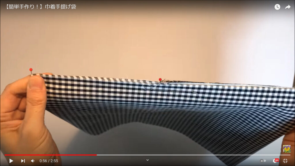表布と内布のサイドを合わせる作業を解説している動画で、布を手に持ち、サイドをピンで留めた様子を表示した画像。