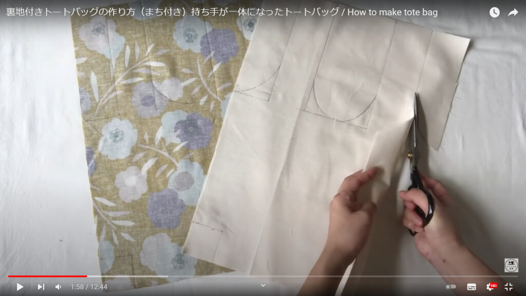 用意したトートバッグの表地と裏地を製図に合わせて裁断する作業を解説している動画で、生地に書いた線に沿ってハサミで裁断している画像。
