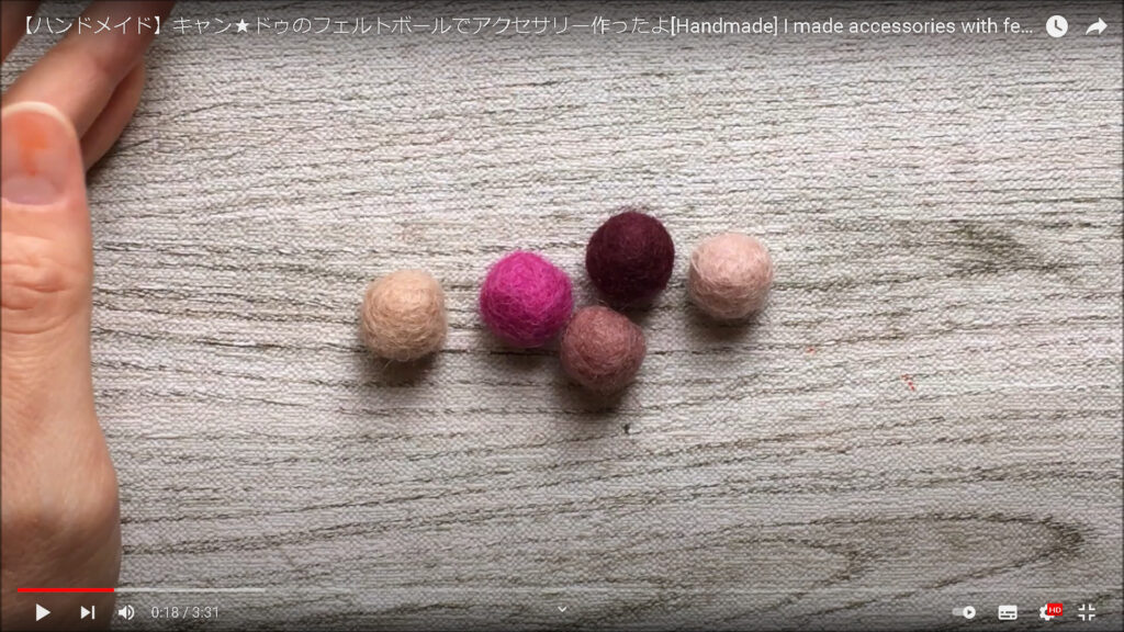 木製テーブルの上に、5つのフェルトボールが置いてある場面。ボールの色は右からそれぞれ、ベージュ、こげ茶色、茶色、ピンク、ベージュ。
