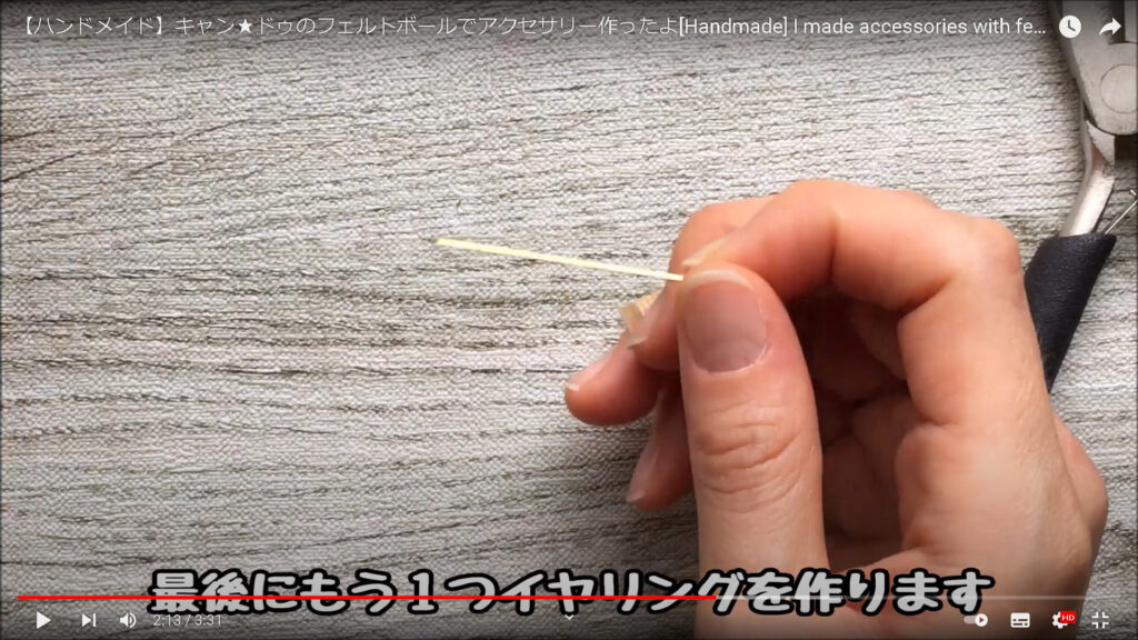フェルトボールを使ったイヤリングの作り方を紹介する場面。画面には、イヤリングに使うピンを持っているところが映し出されている。
