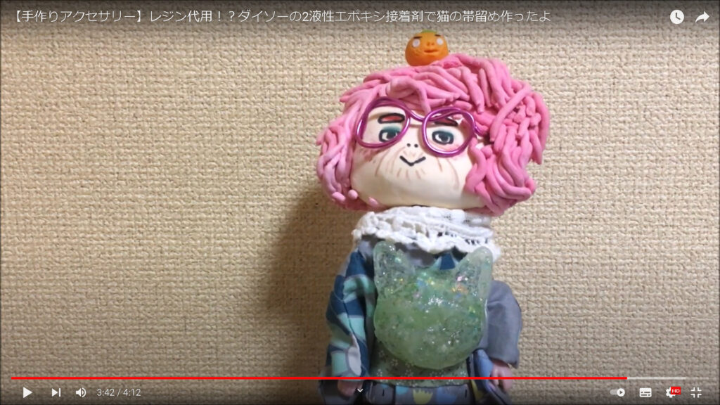 動画の終盤にて、作品についての総括を行う場面。チャンネルのオリジナルキャラクターであるピンク色の髪をしたおばあさんの人形が、完成した作品を付けているのが分かる。