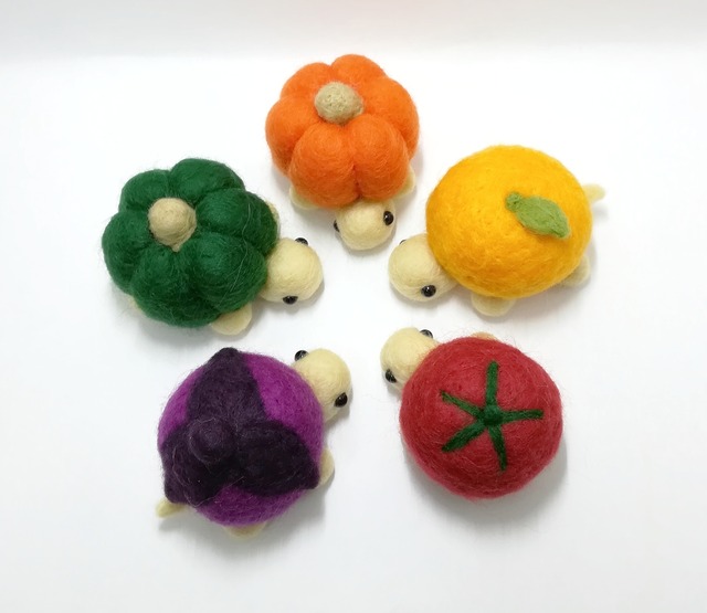 羊毛フェルトでできた甲羅が野菜のカメ（かぼちゃ、みかん、ナス、トマト）が円になって集まっている様子。