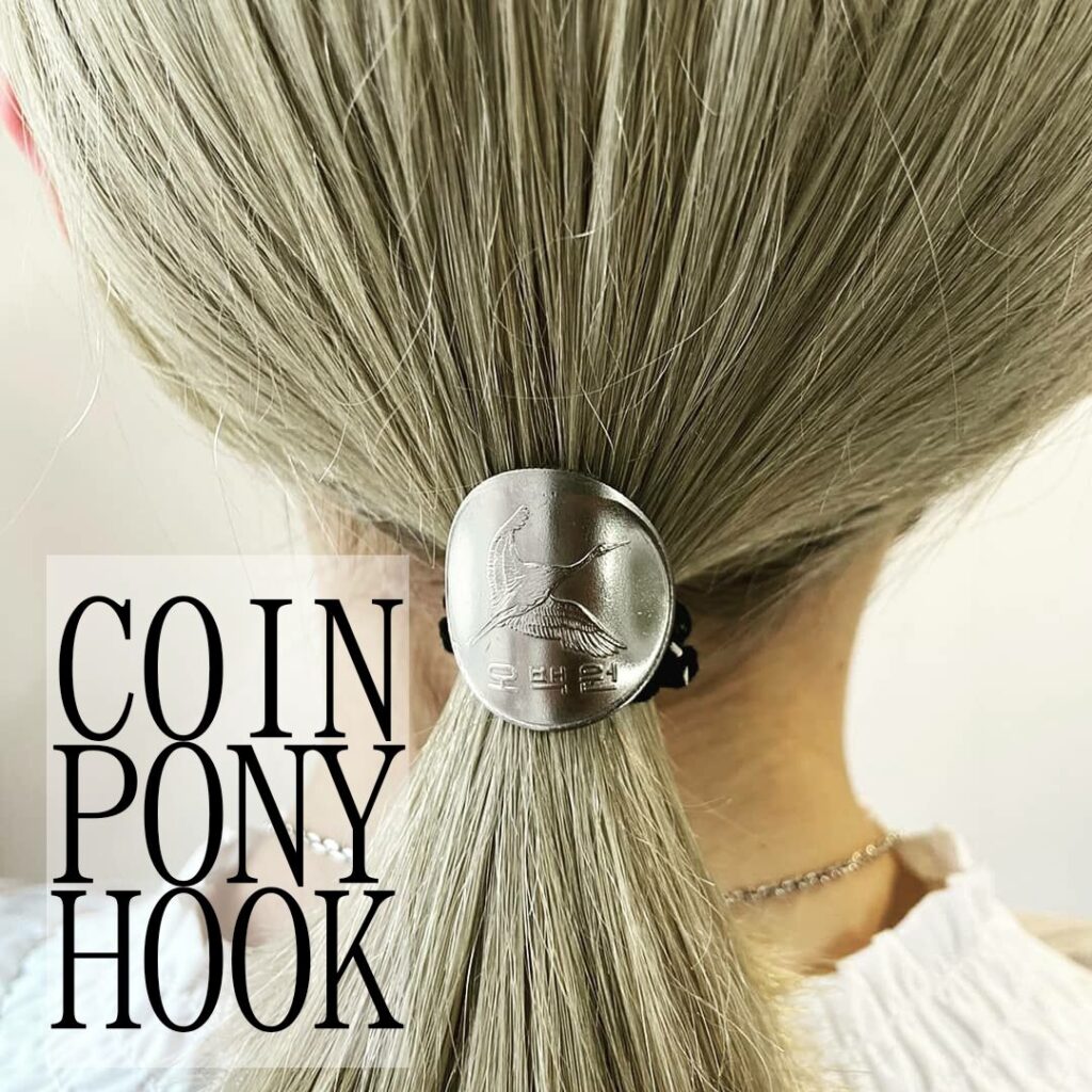 画像は作品を映している様子です。
コインで作られたポニーフックを金髪の女性が使用しています。
作品はアップで映されていて、左隣には編集で「COIN PONY HOOK」とテキストが入っています。