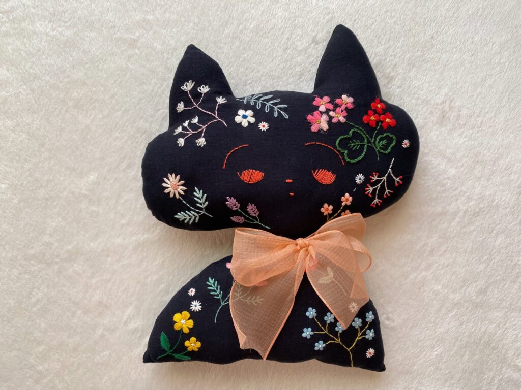 黒い猫の人形。顔の周りや体にお花の刺繍がたくさんある。