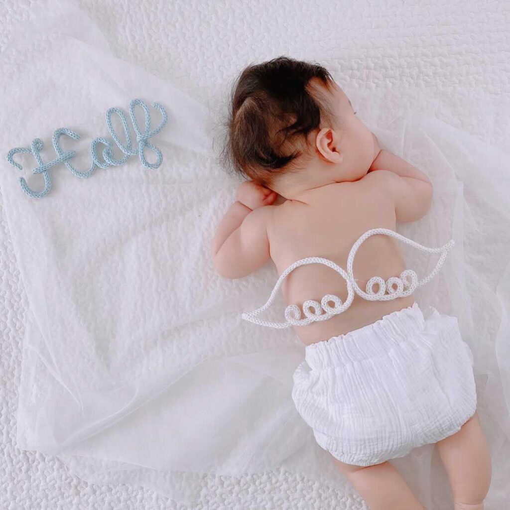 白いタオルケットの上に赤ちゃんがねころんでいる。背中にウールレターの羽が置いてある。