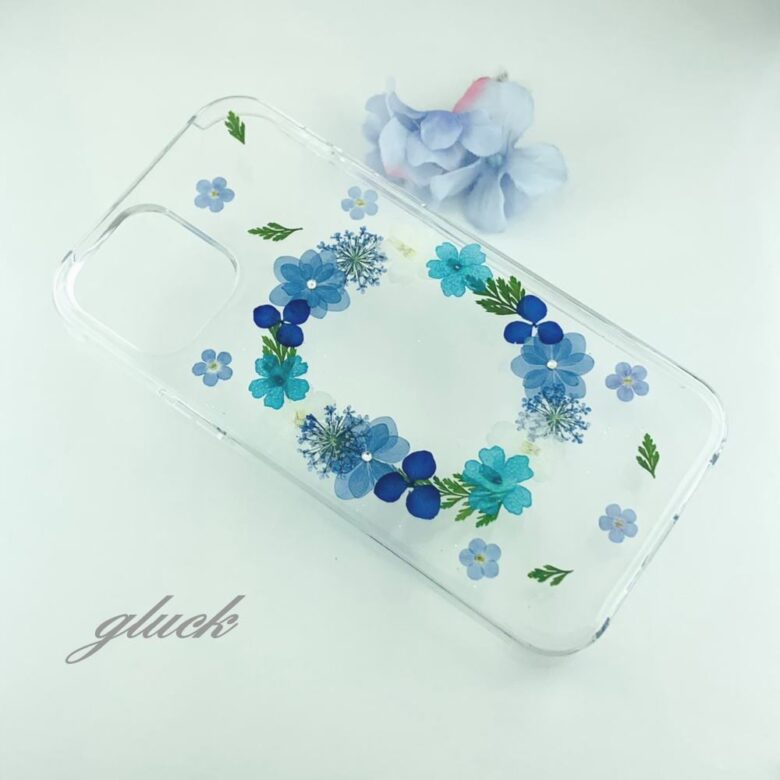 透明のスマホケースにブルーと水色の小花が円に飾られている。