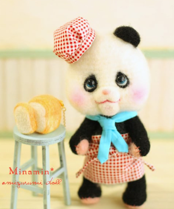 パン屋の恰好をしたパンダの編みぐるみの写真。パンを売っている様に置かれている様子。