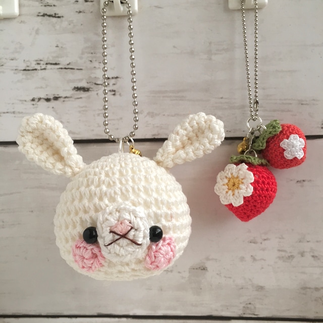 白くて丸いウサギの顔と、小さな白い花がついたイチゴのストラップが2点並んでいる画像。