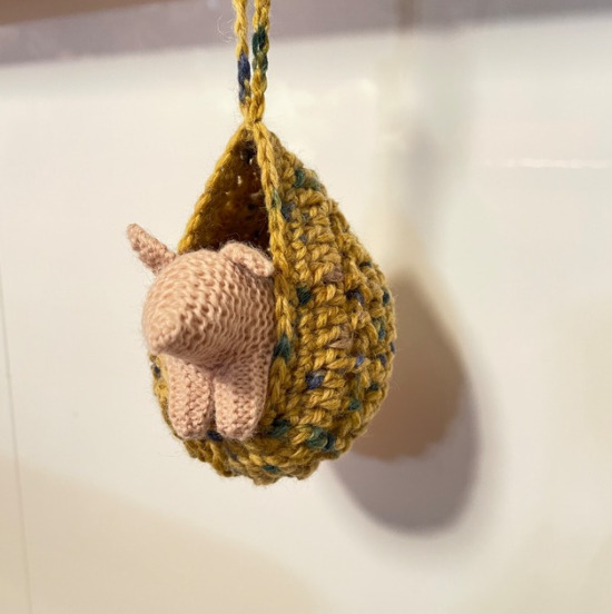 椅子型ハンモックに豚の編みぐるみが入っている様子の写真。壁に吊るされている様子。