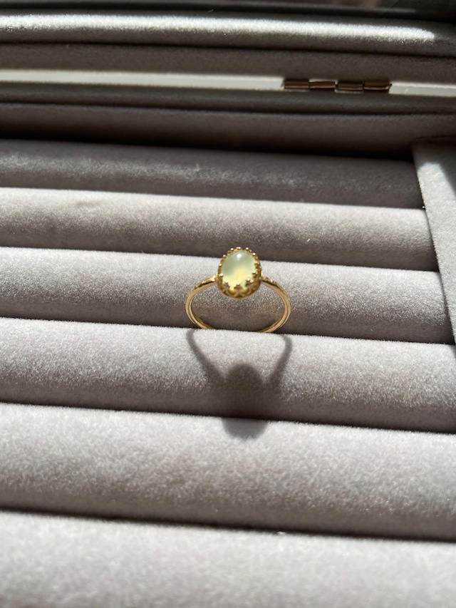 光を浴びて淡いグリーンに輝く、カボションカットの天然プレナイトを1石留めたゴールドカラーのリングの画像。