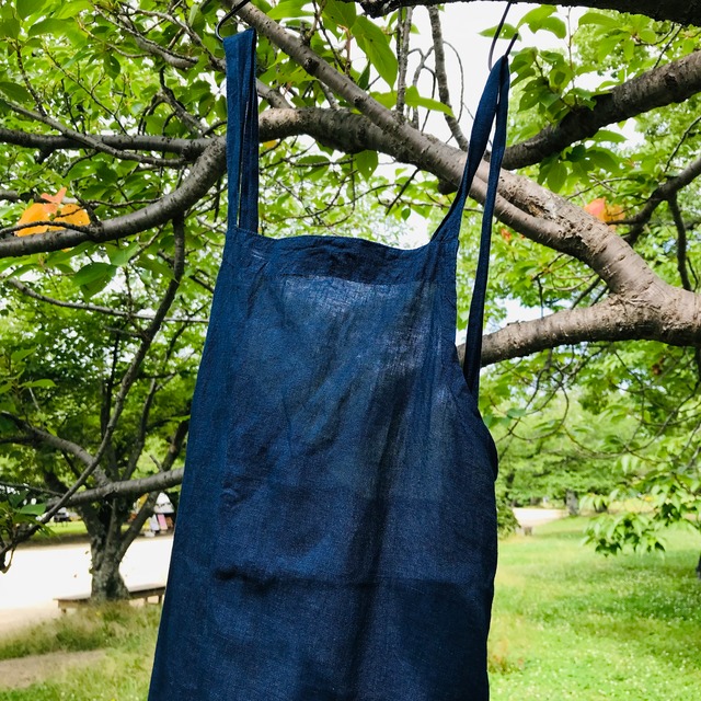 本藍染されたエプロンの写真。エプロンの全体が見えるように、木の枝に掛けられている様子。