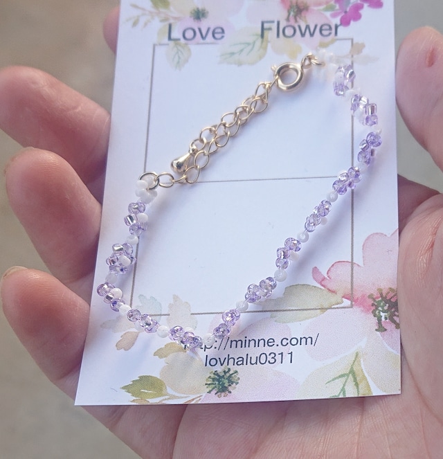 淡い紫と白のビーズで編んだお花のブレスレットの画像。金具はゴールドカラーでアジャスターが付きサイズを調整できるようになっている。