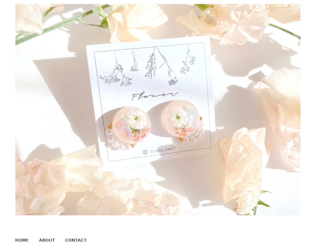 東山優衣さんのショップのトップ画像。白い花が封入され、ほんのりピンクに色づいた丸いイヤリング作品が大きく表示されている。