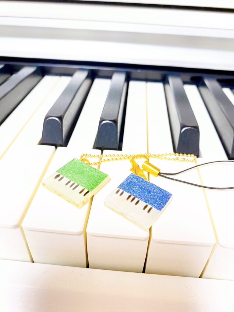 「ピアノキーホルダー　キラキラ四角」という商品の写真。実際のピアノの上にキーホルダーが置かれている。