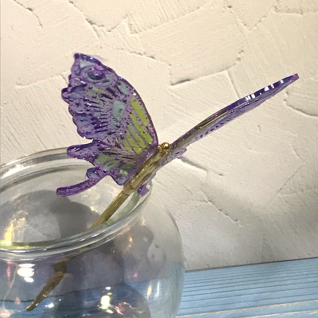「虹色胡蝶のかんざし」という商品の写真。かんざしを瓶に挿し、蝶がよく見えるように置かれている様子。