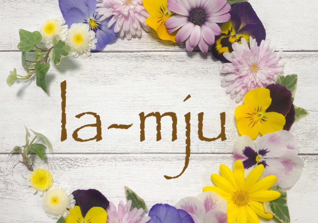 福元美幸さんのショップLa-mjuのトップ画像、木目背景の上に花が円形に飾られ、真ん中にショップ名が書かれている