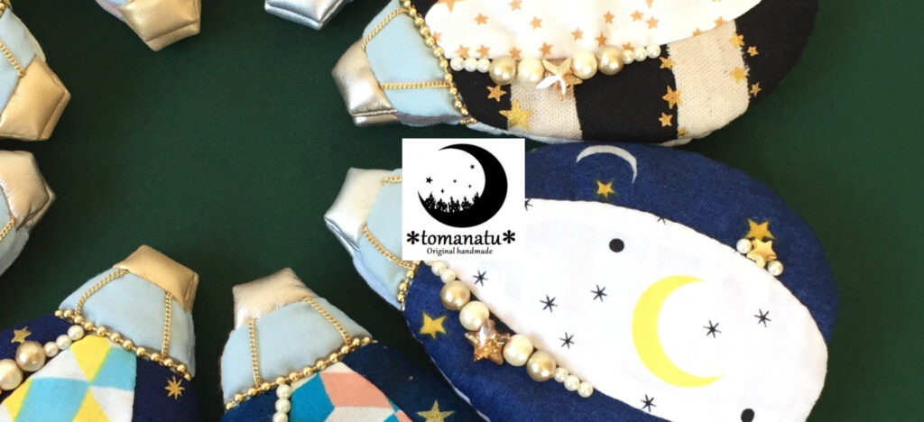 藤原暢子さんのショップ＊tomanatu＊のトップ画像、気球モチーフの布小物の写真にショップ名と月の絵が描かれている