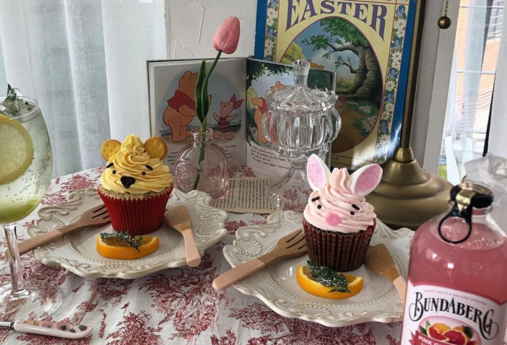 村川亮太さんのショップchimuのトップ画像、テーブルの上にクマのプーさんのキャラクターカップケーキが二つ置かれている。そのほかにも本やチューリップ、飲み物が置かれている。