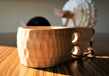 木の机の上に木彫りでできたマグカップが置かれている。カップの持ち手には丸く二か所穴が空いている。