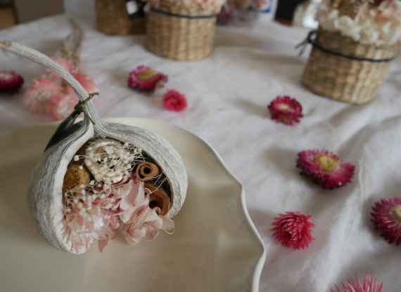 白い皿の上に白いブッダナッツが置かれている。ブッダナッツの中には薄ピンクや白の花が飾られている。皿の周りには赤やピンクのドライフラワーが散りばめられている。