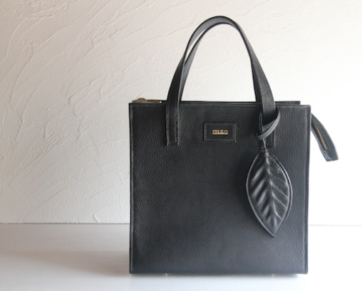 黒いレザーのショルダーバッグ。持ち手には葉っぱのデザインのレザーチャームがついている。