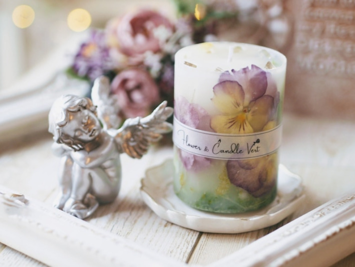 フレームやお花、天使の置物の横にお皿に乗ったお花のキャンドルが飾られている。
キャンドルには紫のパンジーや緑が入っている。キャンドルの上には黄色い天然石が乗っている。