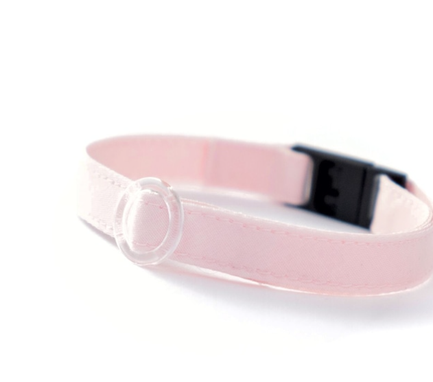 白の背景にピンク色の猫の首輪が置かれている。首輪のトップには透明のサークルパーツ、留め具は黒色がついている。