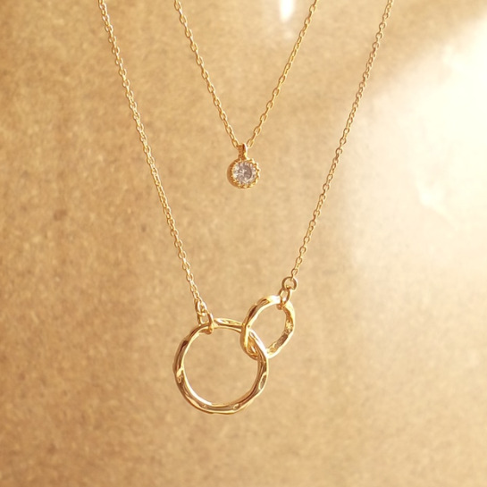 ゴールドの一粒ネックレスと、トップにリングが二つ絡まったゴールドネックレスが写っている。