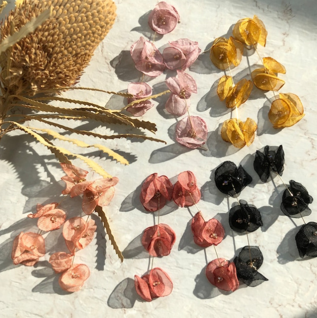テーブルの上にお花デザインのピアスが五種類並んでいる。ピンク、ブラック、黄色など、お花が三つ並んだデザインになっている。