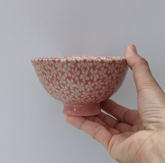 花びらが白、真ん中が黄色いお花が散りばめられたピンクの茶碗を持っている手が写っている
