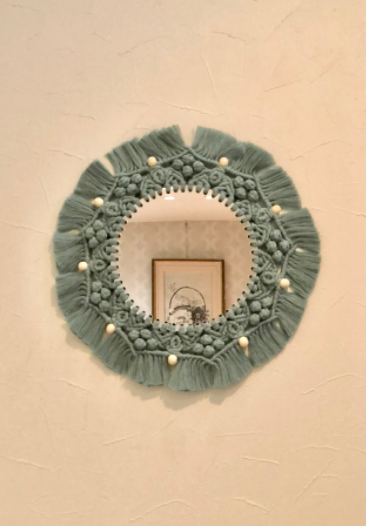 壁に円形のミラーが飾られている。ミラーの周りにはくすみブルーのマクラメ編みが施されている。