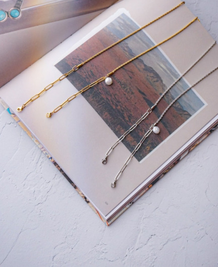 写真の本の上に、ゴールドとシルバーのマスクチェーンが並べられている。チェーンにはパールが一つついている。