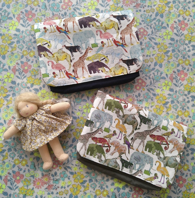 ゾウやキリン、フラミンゴなどの動物の絵が描かれた生地で作られた移動ポケットが二つ並んでおり、その隣にベージュカラーの髪の毛をした女の子の人形が置かれている。