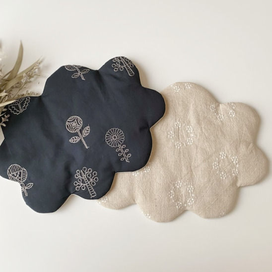 テーブルの上に植物と、ブラックとベージュの雲形刺繍マットが二つ置かれている。マットにはお花の模様が刺繍されている。