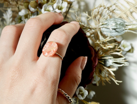 花が飾られたところに手が置かれており、人差し指にピンクのリングをつけている。