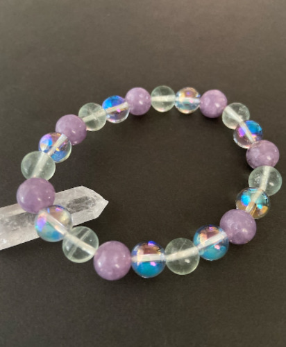 紫、透明、オーロラ色のパワーストーンブレスレットが水晶の上に飾られている