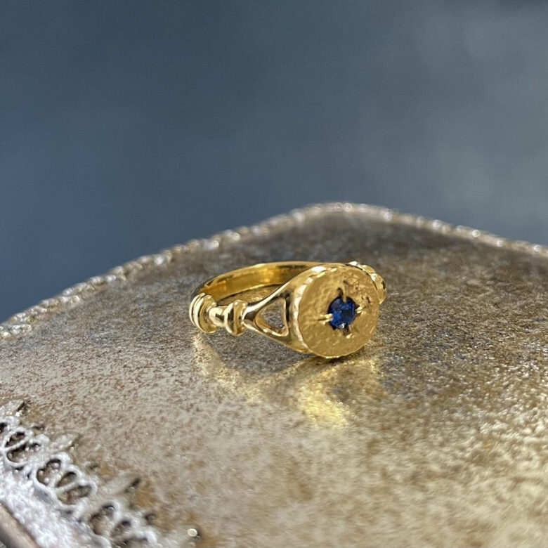 ゴールドメッキを使った指輪です。コインをリングトップに中心には深いブルーの石が入っています。