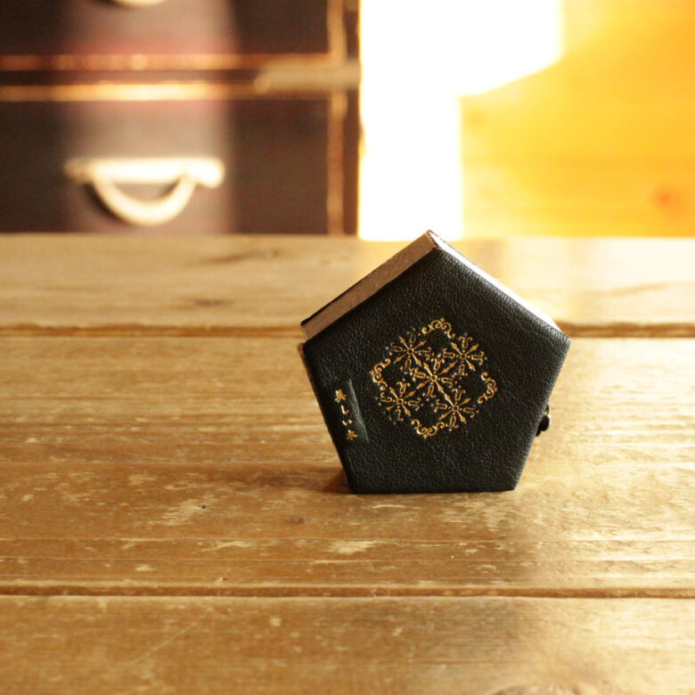 テーブルに置かれた本は、五角形で黒革のカバーに金の箔押しの文様と「美しい本」というタイトルが入っています。