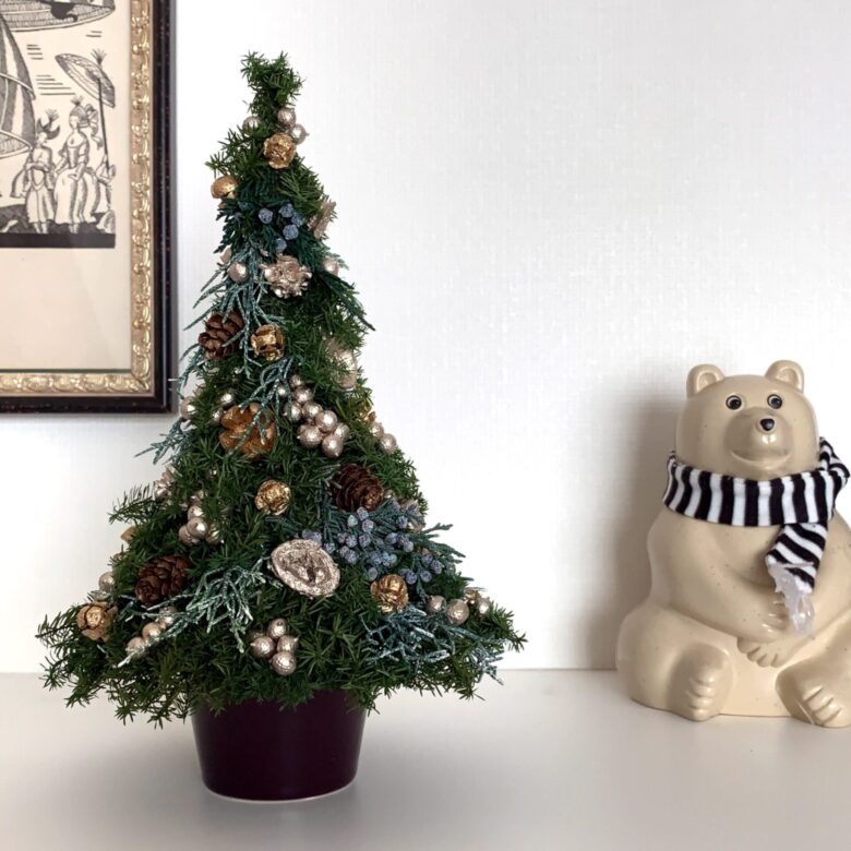 ゴールド・シルバー・ブルー・ブラウンの色バランスが良く、おしゃれなクリスマスツリーです。ツリーの横には、黒と白のボーダー柄のマフラーを着けたクマの置物が飾ってあります。