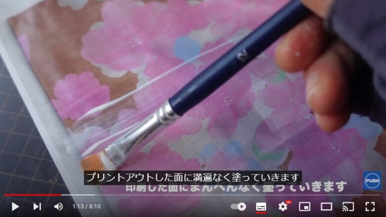 冒頭に画像で紹介された桜柄の紙が画面いっぱいに広がっています。そして、その表面にまんべんなく、筆でデコパージュ専用液を塗っています。