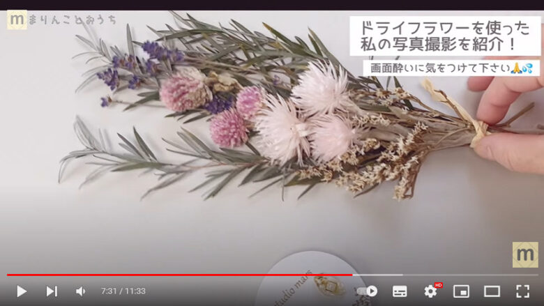 ピンクや紫の花と、細長い緑の葉で作られたミニスワッグを使って、アクセサリ－を撮影しています