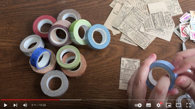 英字スタンプを押したクラフト紙、マスキングテープ、古切手が並べられている。クラフト紙をマスキングテープと古切手を使用して装飾する。