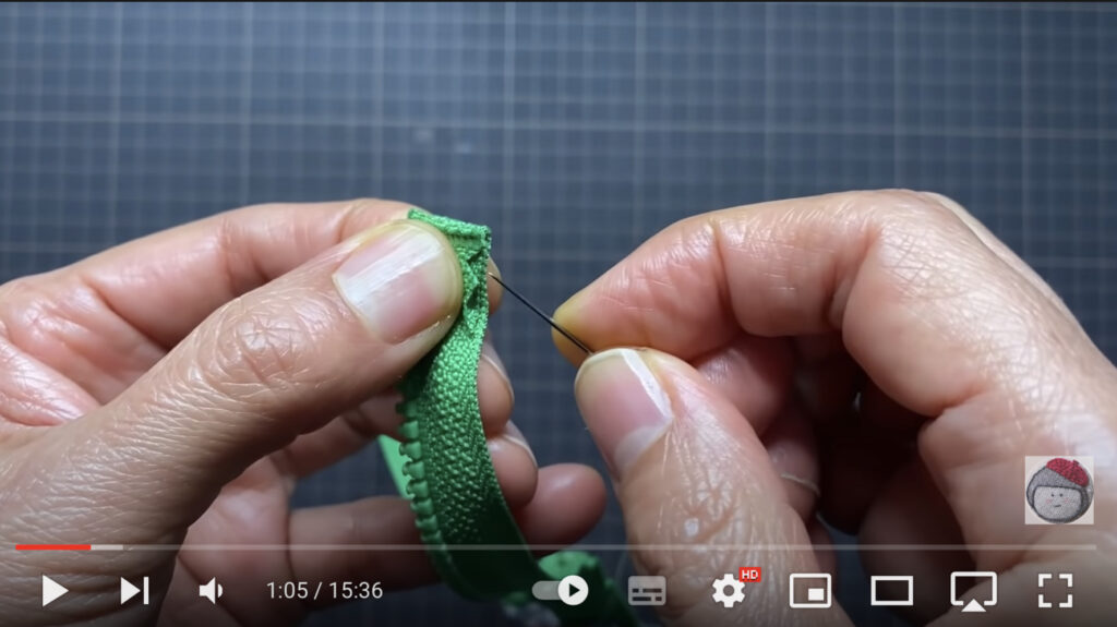 緑色のファスナーの端っこの処理を手縫いでかがっている様子。