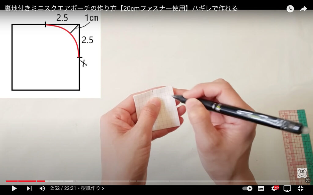型紙を作る手元がアップで映されている。左手に四角い紙を持ち、右手に持った黒いペンで印を描こうとしている。作業台の上には定規が置かれている。画面左上には、描き方の図が表示されている。