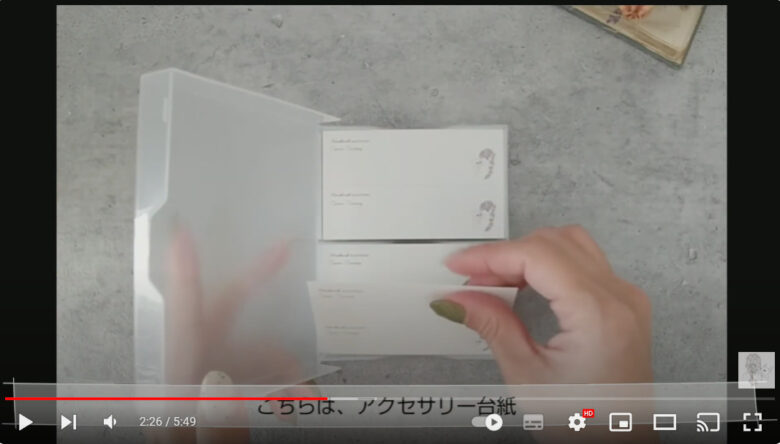 投稿者が実際に使用している、アクセサリーの台紙を公開している場面。台紙はカードケースに収められていて、名刺サイズで色は白。右にイラスト、左に作家名等が記載されている。